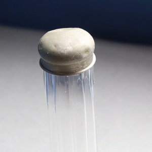 May include: A clear glass bottle with a silver top. The bottle has a ribbed design and is standing on a white surface.