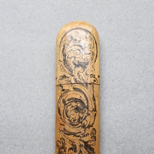 May include: A wooden case with a black and white floral design. The case is closed and has a rounded top and bottom.