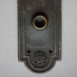 Könnte beinhalten: Eine antike, dunkelbraune Türplatte mit einem dekorativen Blumendesign und einem runden Schlüsselloch. Die Platte hat einen abgenutzten, alten Look.