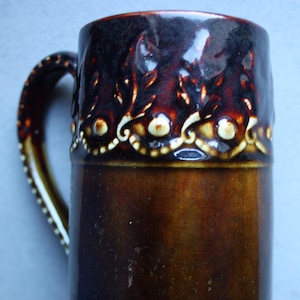 May include: A brown ceramic mug with a white and brown design. The mug has a handle and a wide base.