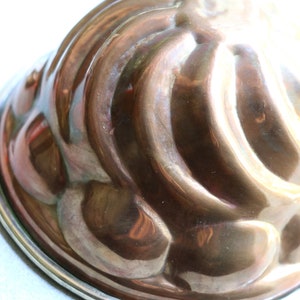 Puede incluir: Un molde de cobre vintage para hacer un pastel bundt o un molde de gelatina. El molde tiene un dise&ntilde;o acanalado y un borde plateado.
