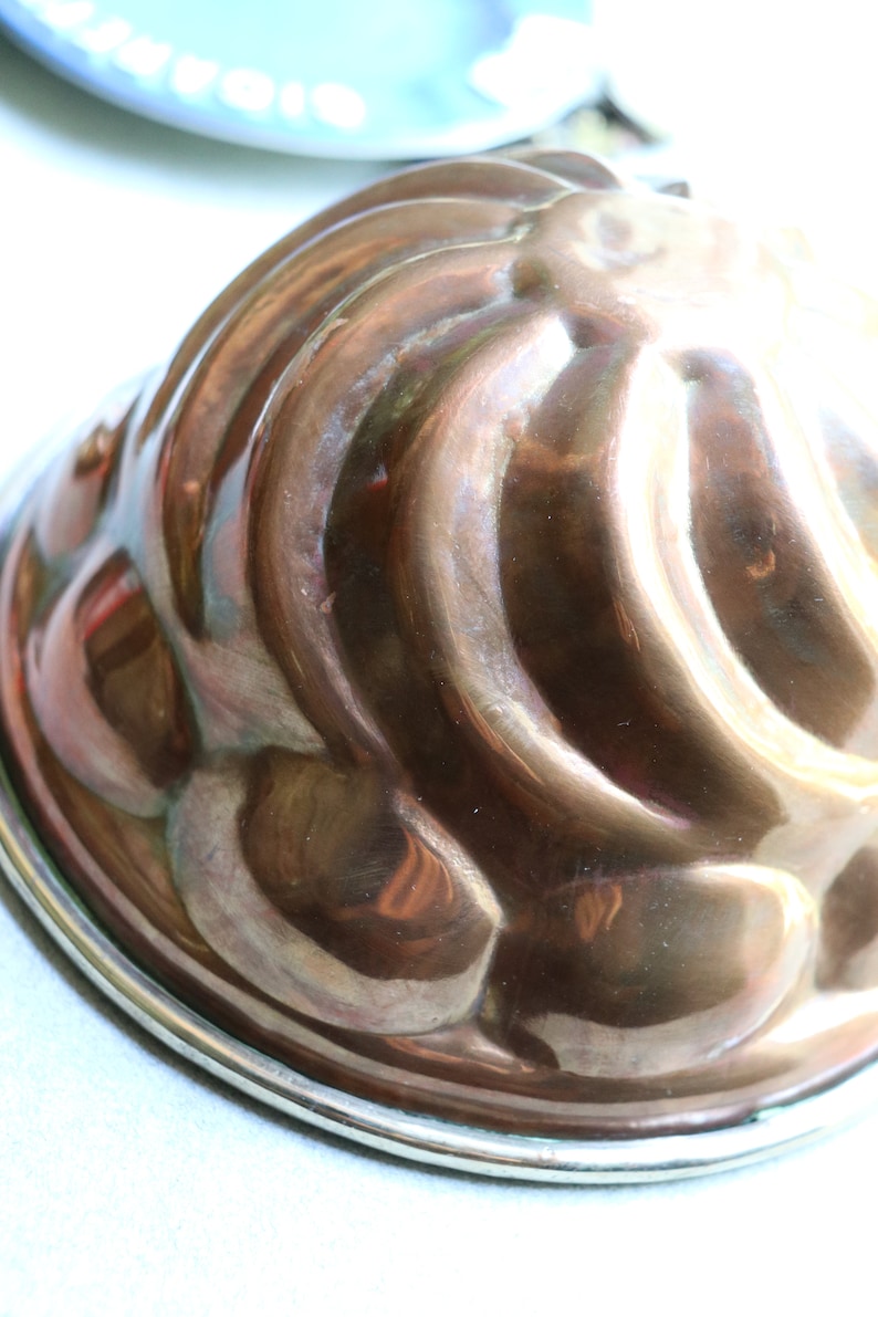 Puede incluir: Un molde de cobre vintage para hacer un pastel bundt o un molde de gelatina. El molde tiene un dise&ntilde;o acanalado y un borde plateado.