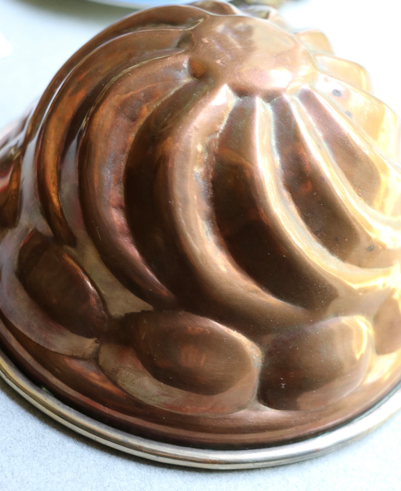 Puede incluir: Un molde de gelatina de cobre vintage con un dise&ntilde;o acanalado y un borde plateado.