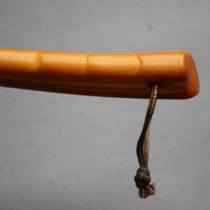 May include: A close-up of the handle of a walking stick. The handle is made of a light brown material with a smooth, polished finish. A brown cord is attached to the handle.