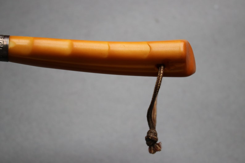 May include: A close-up of the handle of a walking stick. The handle is made of a light brown material with a smooth, polished finish. A brown cord is attached to the handle.