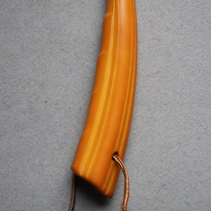 May include: A yellow and orange striped handle with a silver band and a Greek key design. The handle is attached to a brown cord.