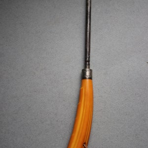 May include: A vintage knife with a brown metal blade and a yellow and orange striped handle. The handle has a silver band with a decorative pattern. A brown cord is attached to the handle.