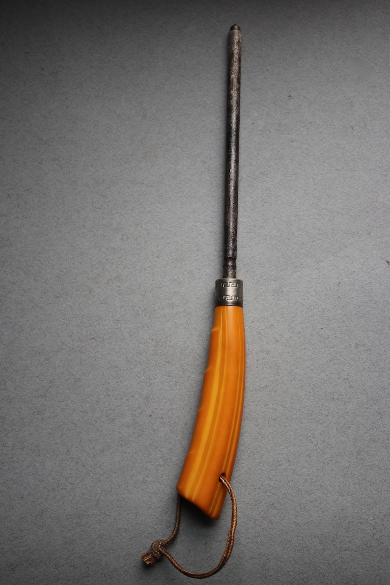 May include: A vintage knife with a brown metal blade and a yellow and orange striped handle. The handle has a silver band with a decorative pattern. A brown cord is attached to the handle.