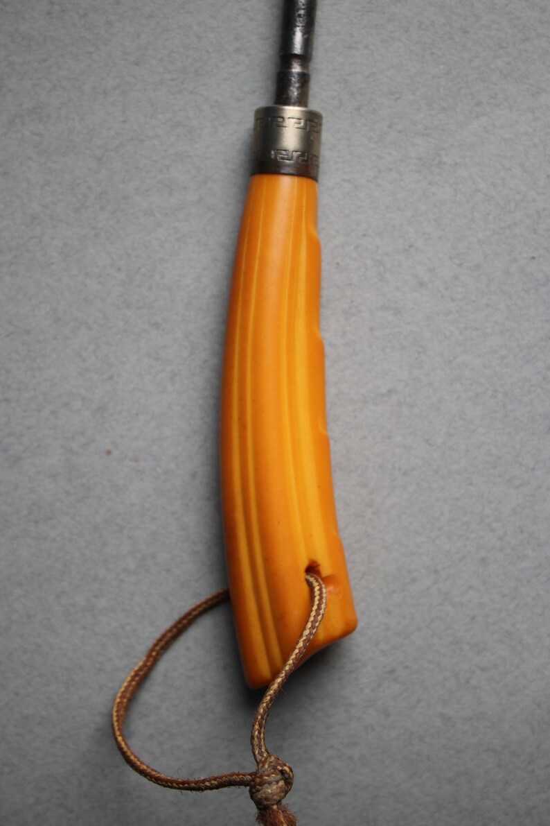 May include: A yellow and brown striped handle with a silver band and a black metal tip. The handle has a brown leather cord attached to it.