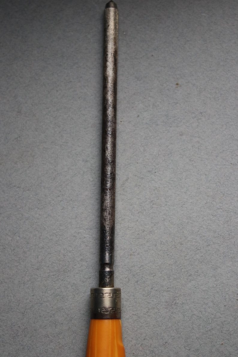 May include: A metal knife sharpener with a brown wooden handle. The handle has a silver band with a decorative pattern.