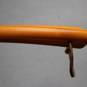 May include: A close-up of a yellow, wooden walking stick handle with a brown cord attached.