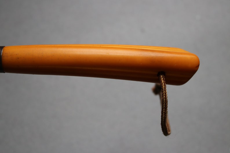 May include: A close-up of a yellow, wooden walking stick handle with a brown cord attached.