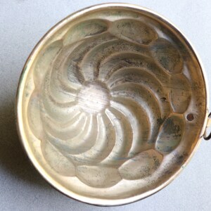 Puede incluir: Un molde para pastel de metal plateado vintage con un dise&ntilde;o acanalado. El molde tiene una peque&ntilde;a manija en el lateral.