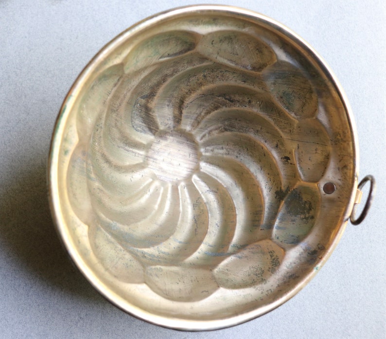 Puede incluir: Un molde para pastel de metal plateado vintage con un dise&ntilde;o acanalado. El molde tiene una peque&ntilde;a manija en el lateral.