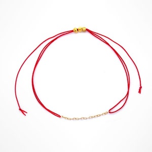 May include: A red string bracelet with gold beads and a gold chain.