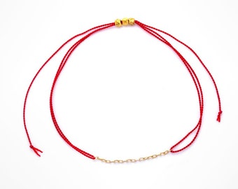 Pode incluir: Um bracelete de corda vermelha com contas douradas e uma corrente dourada.