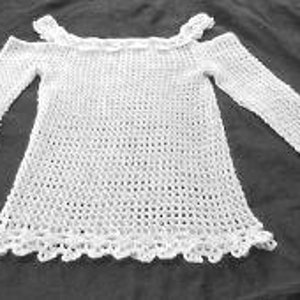 Puede incluir: Top blanco de crochet con un ajuste holgado y mangas largas. El top tiene un escote festoneado y un delicado patrón de calado.