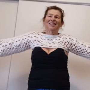 May include: A white crocheted top with a wide, open neckline and long sleeves. The top is made with a delicate, lacy pattern.