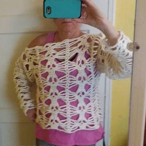 May include: A white crocheted sweater with a skull pattern. The sweater has a loose fit and a wide neckline. The sweater is worn over a pink shirt.
