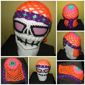 May include: A white crocheted skull mask with orange, pink, and purple accents. The mask has a skull design with eye holes and a mouth opening. The mask is worn on a mannequin head.