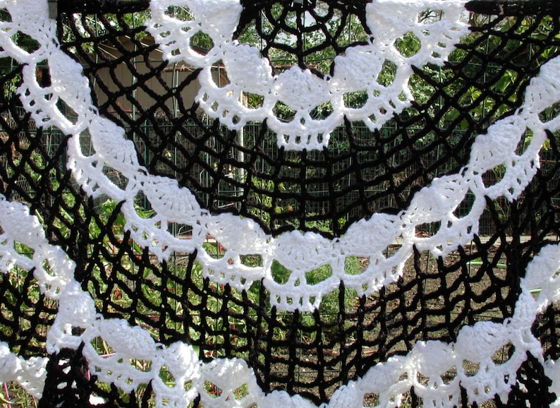 May include: Black and white crocheted skull design. The crochet is in the shape of a half circle with a repeating pattern of skulls.