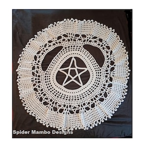 Puede incluir: Doily de ganchillo blanco con una estrella de cinco puntas en el centro. El doily tiene un borde festoneado y un delicado patrón de encaje. "Spider Mambo Designs" está escrito en la esquina inferior izquierda.