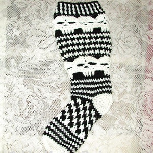Puede incluir: Calienta piernas de crochet blanco y negro con un patrón de calavera. El calienta piernas está hecho con un punto de pata de gallo.
