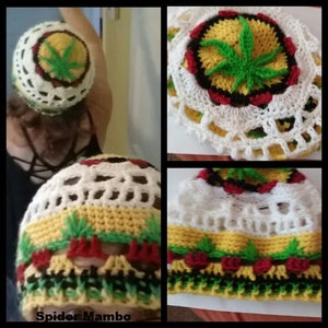 Könnte beinhalten: Eine gehäkelte Mütze mit einem Marihuana-Blatt-Design in Grün, Gelb, Rot und Schwarz. Die Mütze hat einen weißen Häkelrand und ein weißes Häkelband um den unteren Rand. Die Mütze befindet sich auf einem weißen Hintergrund.