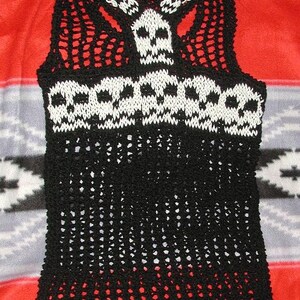 May include: Black crochet top with a white skull design. The top has a wide, open neckline and a loose fit.