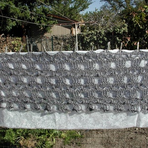 May include: A gray crocheted shawl with a lacy pattern hangs on a clothesline.