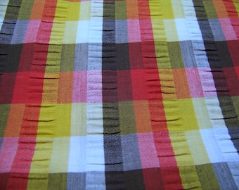 May include: A close-up of a fabric with a checkered pattern in red, yellow, white, and black. The fabric has a textured, woven look.