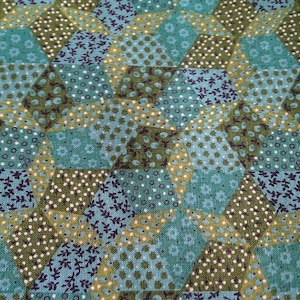 May include: Close-up of a fabric with a geometric pattern. The design features a patchwork of hexagonal shapes in shades of teal, olive green, and cream. Each hexagon is filled with floral and polka dot patterns.