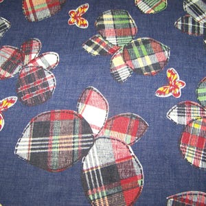 May include: A navy blue fabric with a repeating pattern of plaid flower shapes and butterfly appliqués. The plaid incorporates red, black, white, and yellow. The butterflies are red, yellow, and white.