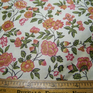 May include: A white fabric with a repeating pattern of pink and orange flowers with green leaves. The fabric is measured with a wooden ruler.