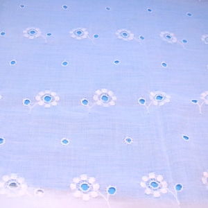 May include: White eyelet fabric with a light blue background. The fabric has a repeating pattern of small white flowers.