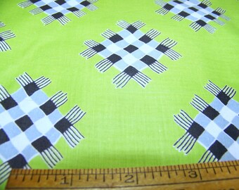 May include: Green fabric with a repeating pattern of black and white checkered squares with a fringe border. A wooden ruler is in the foreground.