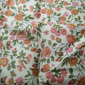 May include: A white fabric with a repeating pattern of pink and yellow flowers with green leaves. The fabric has a vintage feel.