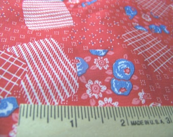 May include: Close-up of a red fabric with white and blue floral and geometric patterns. The fabric features white stripes, grids, and small dots. A ruler with inch measurements is at the bottom.