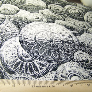 May include: Black and white fabric with a repeating circular pattern. The design features detailed, dotted illustrations of stylized floral and geometric shapes. A wooden ruler with inch markings is in the foreground, indicating the scale of the fabric.