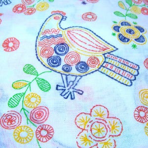 May include: White fabric with a colorful embroidered design featuring a bird and floral patterns. The bird is outlined in yellow with red, blue, and yellow details. Flowers and leaves are in red, yellow, green, and blue.