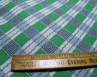 May include: Green and gray checkered fabric with a repeating spiral design. A wooden ruler with the text "Complete Details Buffalo Evening News" is placed on top of the fabric.