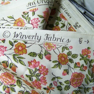 May include: A close-up of white fabric with a floral pattern in shades of pink, orange, and green. The fabric has a label that reads "Waverly Fabrics" and "Good Housekeeping" with a star.
