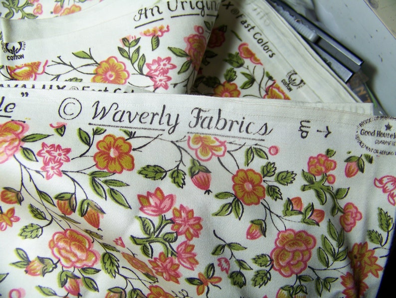 May include: A close-up of white fabric with a floral pattern in shades of pink, orange, and green. The fabric has a label that reads "Waverly Fabrics" and "Good Housekeeping" with a star.