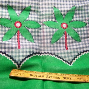 May include: Green and white gingham fabric with a repeating pattern of green palm trees. The fabric has a black and white zig-zag trim along the bottom edge. A wooden ruler with the text "BUFFALO EVENING NEWS" is placed on the fabric.