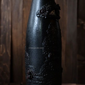 May include: A black glass bottle with a textured, raised design. The bottle is decorated with a black and white pattern.