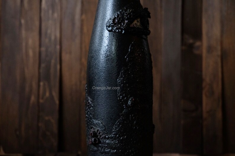 May include: A black glass bottle with a textured, raised design. The bottle is decorated with a black and white pattern.