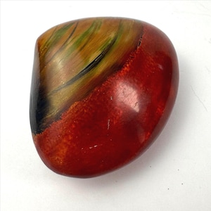May include: A polished, rounded stone featuring a vibrant color palette of deep red, earthy brown, and streaks of forest green. The surface has a smooth, glossy finish with distinct color transitions and natural mineral patterns visible throughout.