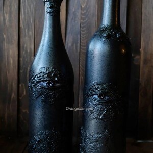 May include: Two black glass bottles with a textured surface and an eye design. The bottle on the left is labeled "Bottle Style: Burgundy" and the bottle on the right is labeled "Bottle Style: Bordeaux".