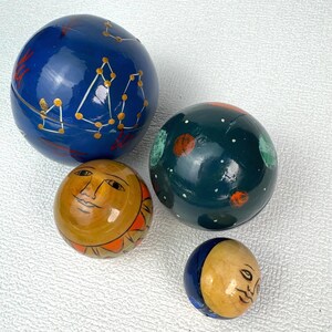 May include: Four spherical objects with celestial designs. One large blue sphere features gold constellations. A medium dark green sphere displays orange planets and white stars. A yellow sphere shows a sun face, and a small blue and yellow moon sphere.