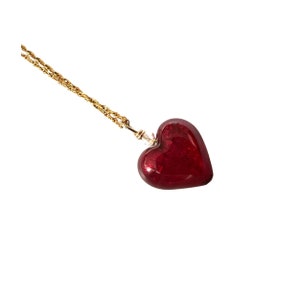 May include: A gold chain necklace with a red glass heart pendant.
